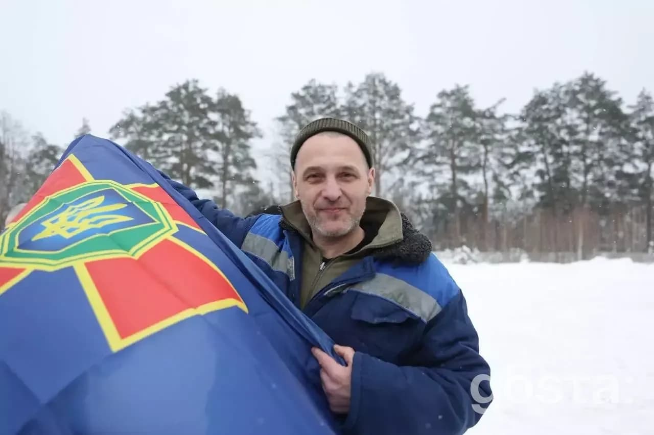 Військовослужбовець з українським прапором на фоні засніжених дерев, повернення 157 захисників додому.