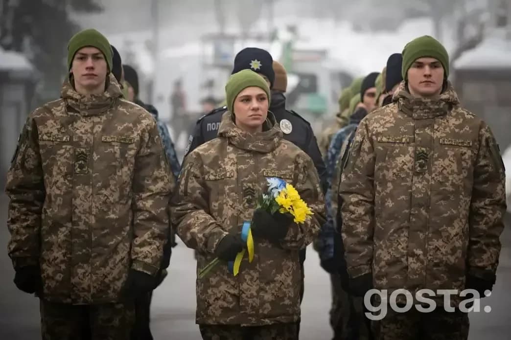 Троє українських військових у камуфляжі з квітами вшановують пам'ять Героїв Крут у Києві.