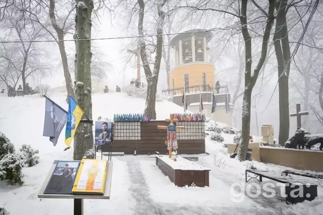 На зображенні зимовий меморіал Героїв Крут на Аскольдовій могилі в Києві, прикрашений квітами та прапорами України.