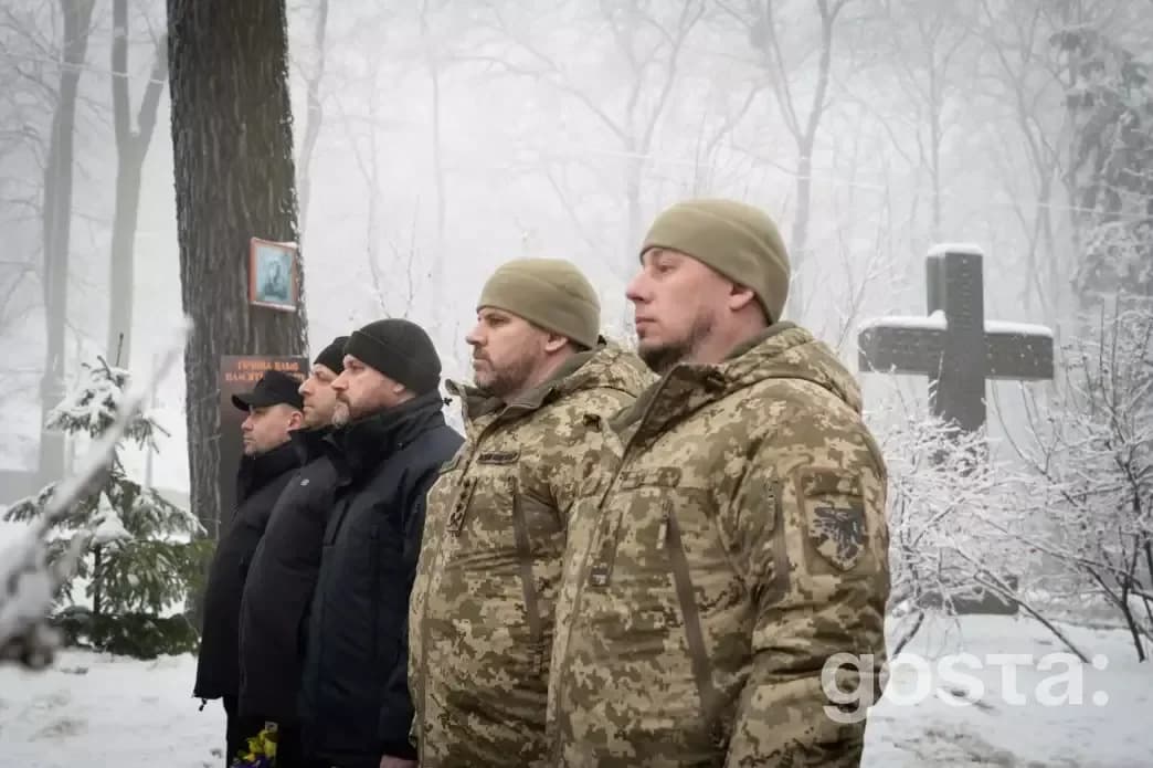 На зображенні люди у військовій формі вшановують пам'ять Героїв Крут біля пам'ятного хреста на Аскольдовій могилі в Києв
