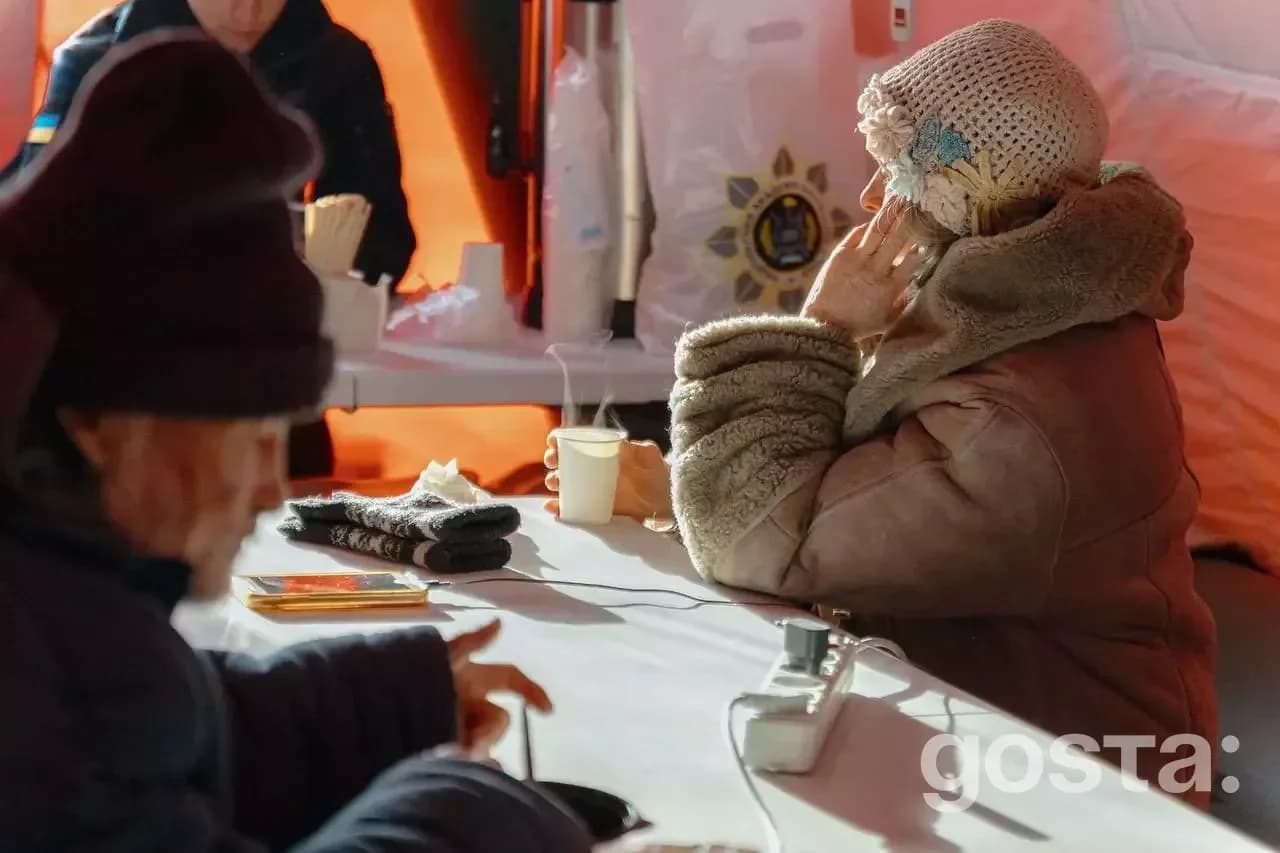 Люди зігріваються у тимчасовому пункті обігріву з напоями та електронікою, організованому для підтримки в холодну пору.