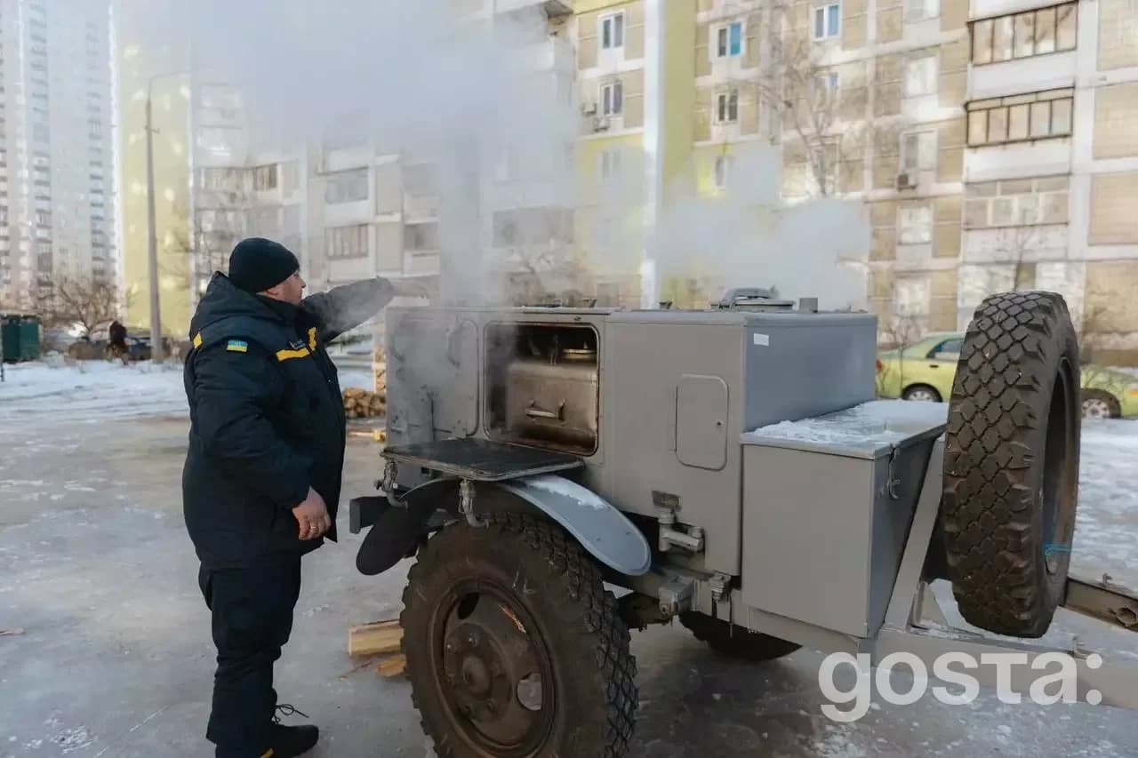 Чоловік у формі біля мобільної пічки в пункті обігріву на вулиці зимового міста.