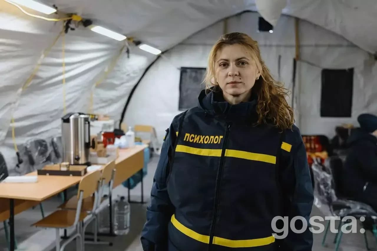 Жінка-психолог у теплому одязі стоїть у наметі обігріву ДСНС, забезпечуючи підтримку постраждалим містянам України.