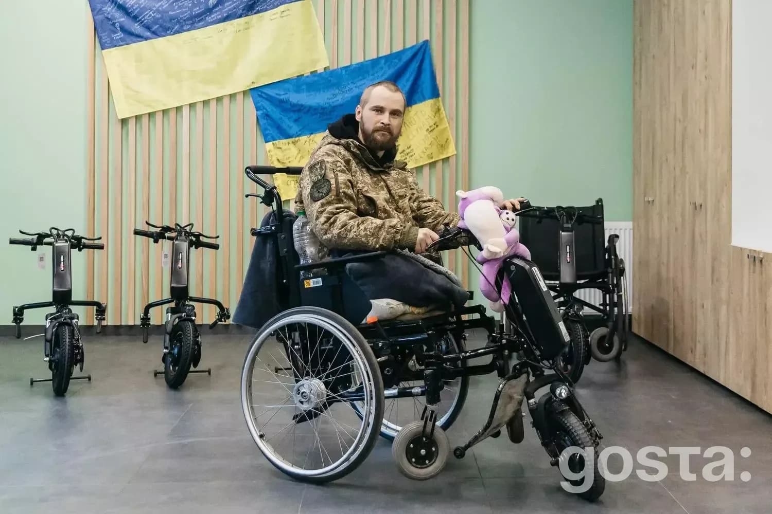 Чоловік у військовій формі на електровізку, поруч прапори України. Реабілітація ветеранів у медцентрі МВС України.