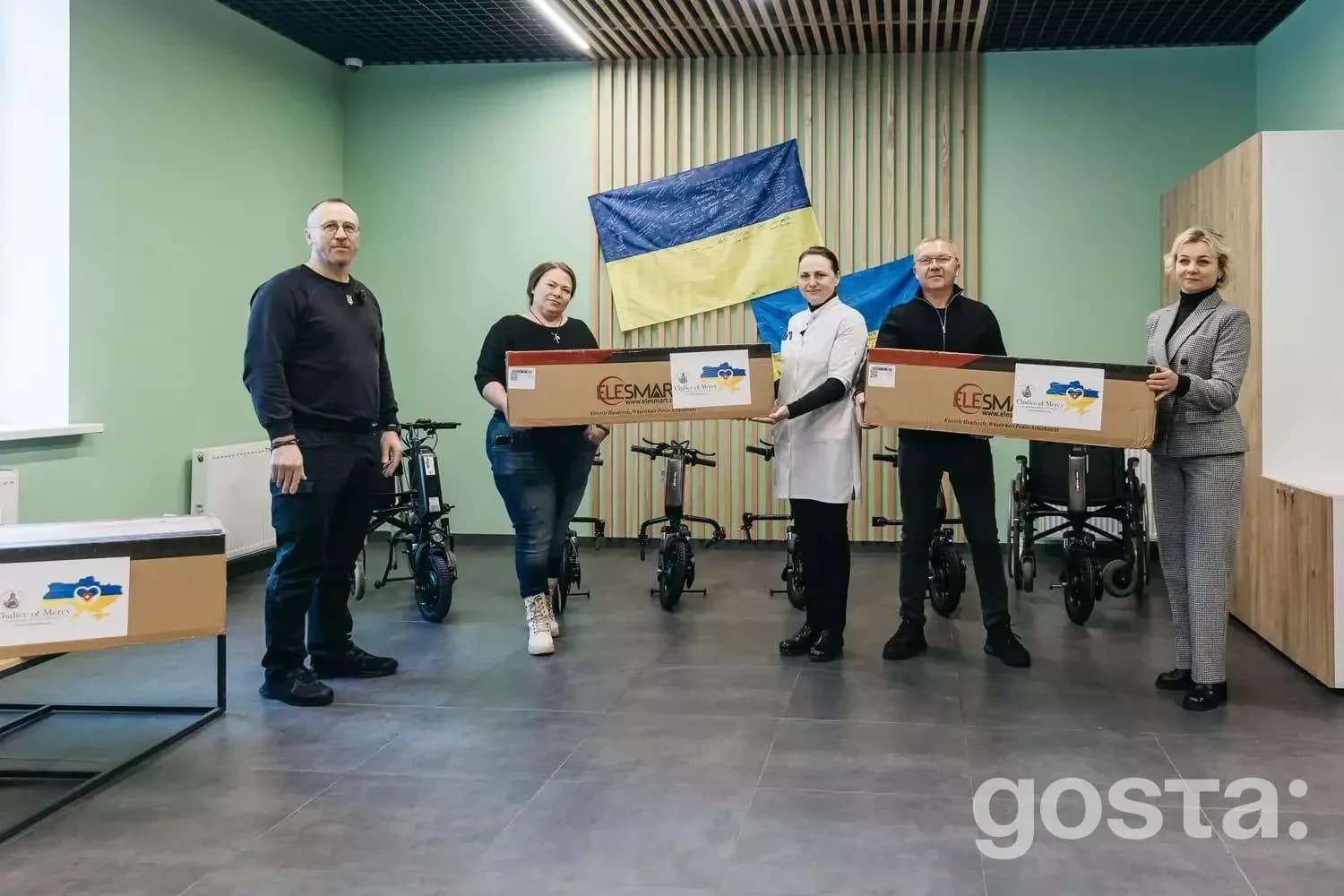Група людей з коробками для електроприводів в медичному центрі з прапором України.