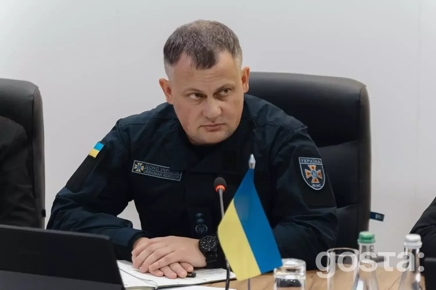На фото зображено високопоставленого офіційного представника України під час зборів за столом, з українським прапором.