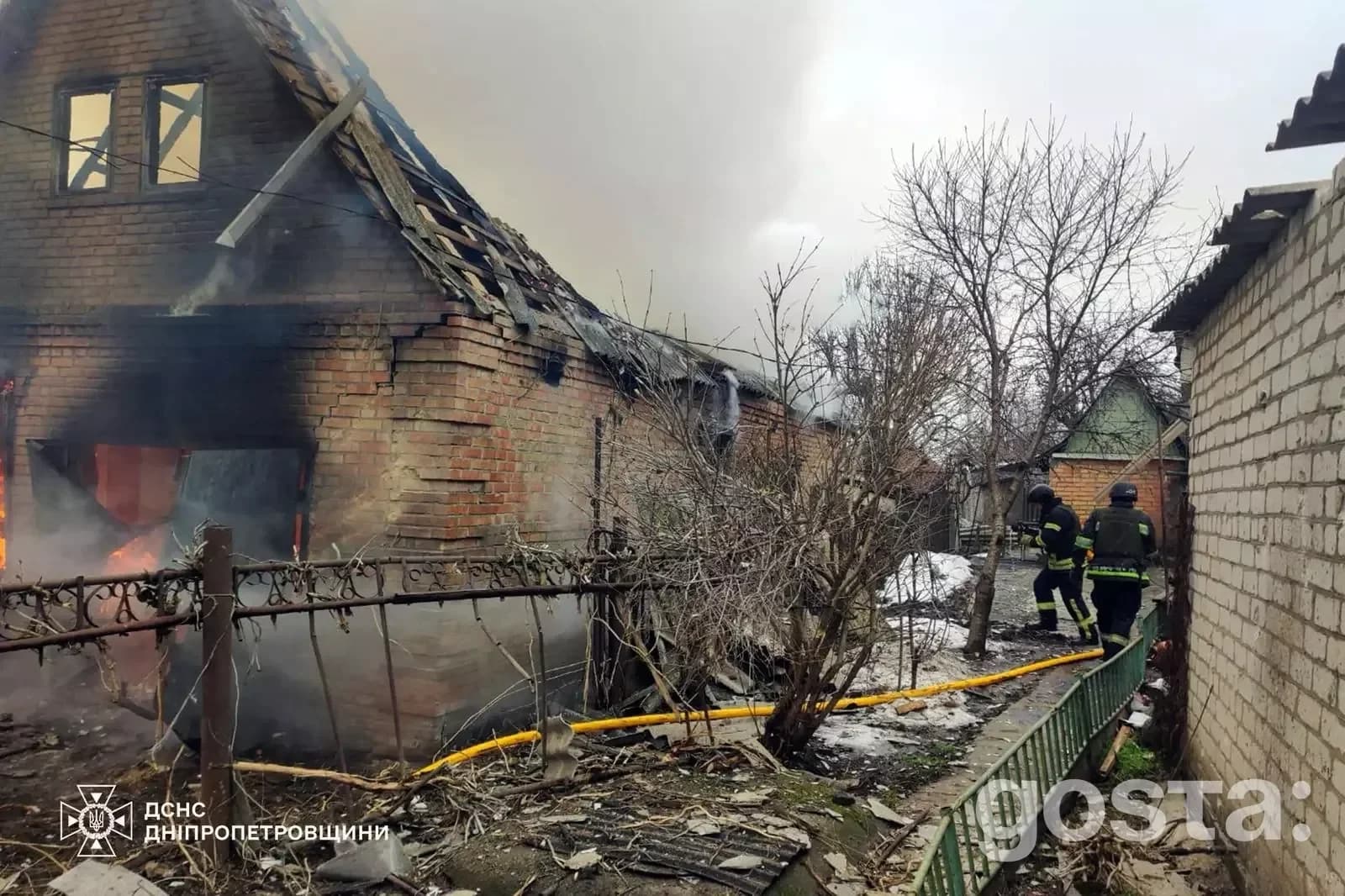 Пожежники гасять палаючий будинок після російського обстрілу в Україні, пошкоджено дах і стіни, дим здіймається в небо.