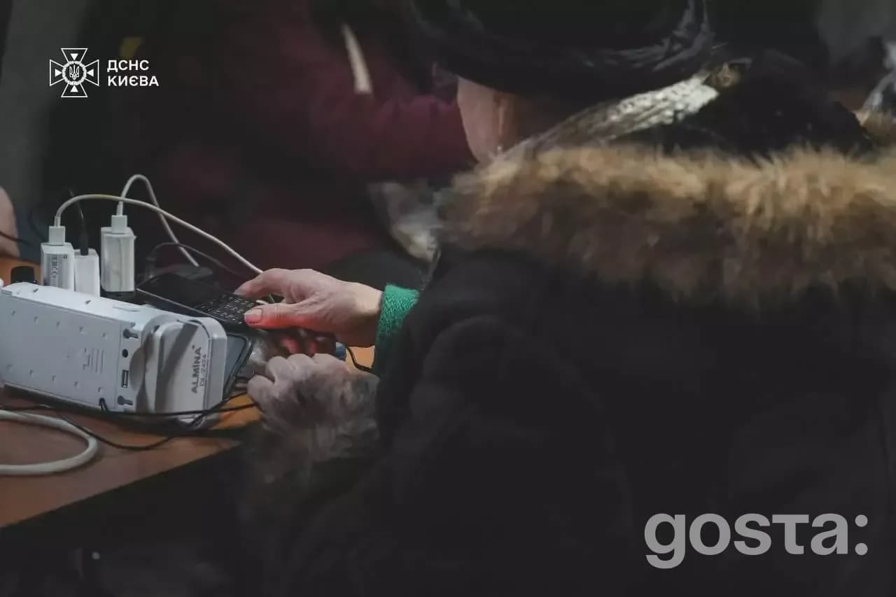 Людина в теплому одязі заряджає пристрій у пункті незламності ДСНС Києва, забезпеченому генератором.