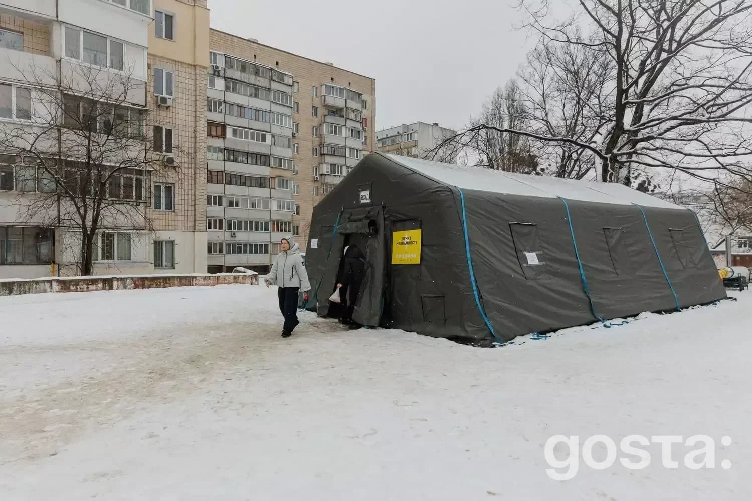 Тимчасовий пункт обігріву в житловому районі, обтяжений снігом, з людьми, які виходять з намету в зимових умовах.