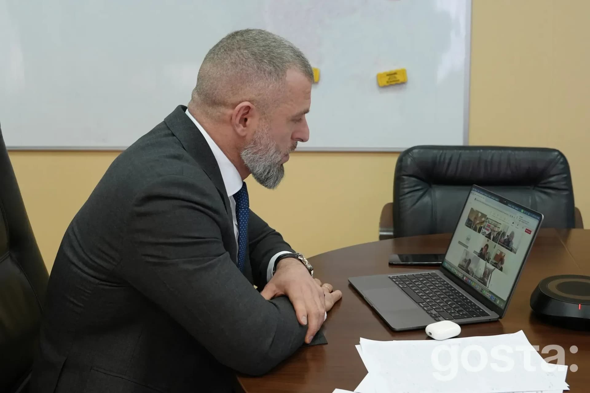 На фото зображено людину, яка бере участь в онлайн-зустрічі, сидячи за столом з ноутбуком.