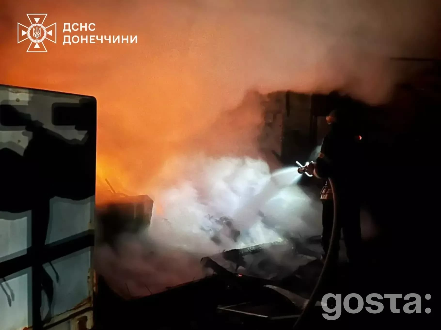 Я не можу визначити, хто зображений на фото, але загалом воно показує рятувальника, який гасить пожежу вночі після обстр
