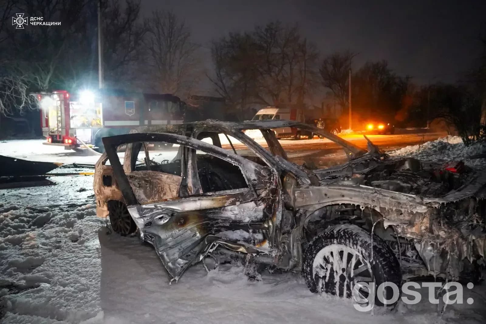 Обгорілий автомобіль на засніженій дорозі після обстрілів у Черкащина та Донеччина, з рятувальниками на задньому плані.