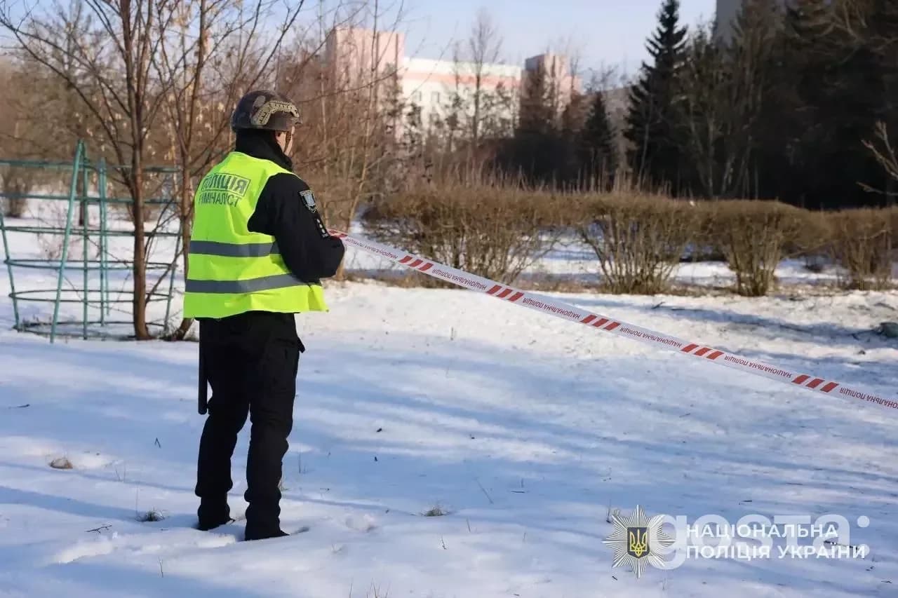 Поліцейський обстежує територію після російських атак на Київщині, зима, стрічка огорожі на снігу.