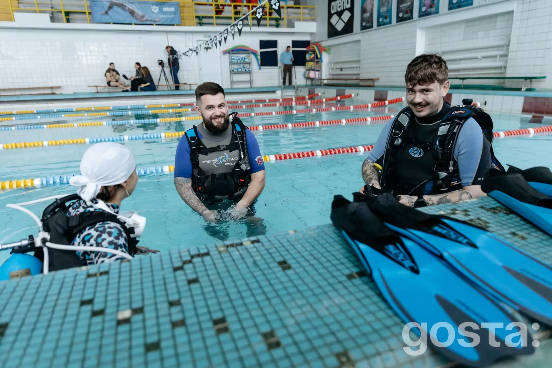 На зображенні троє людей у басейні займаються дайвінгом для реабілітації військових, один інструктор.