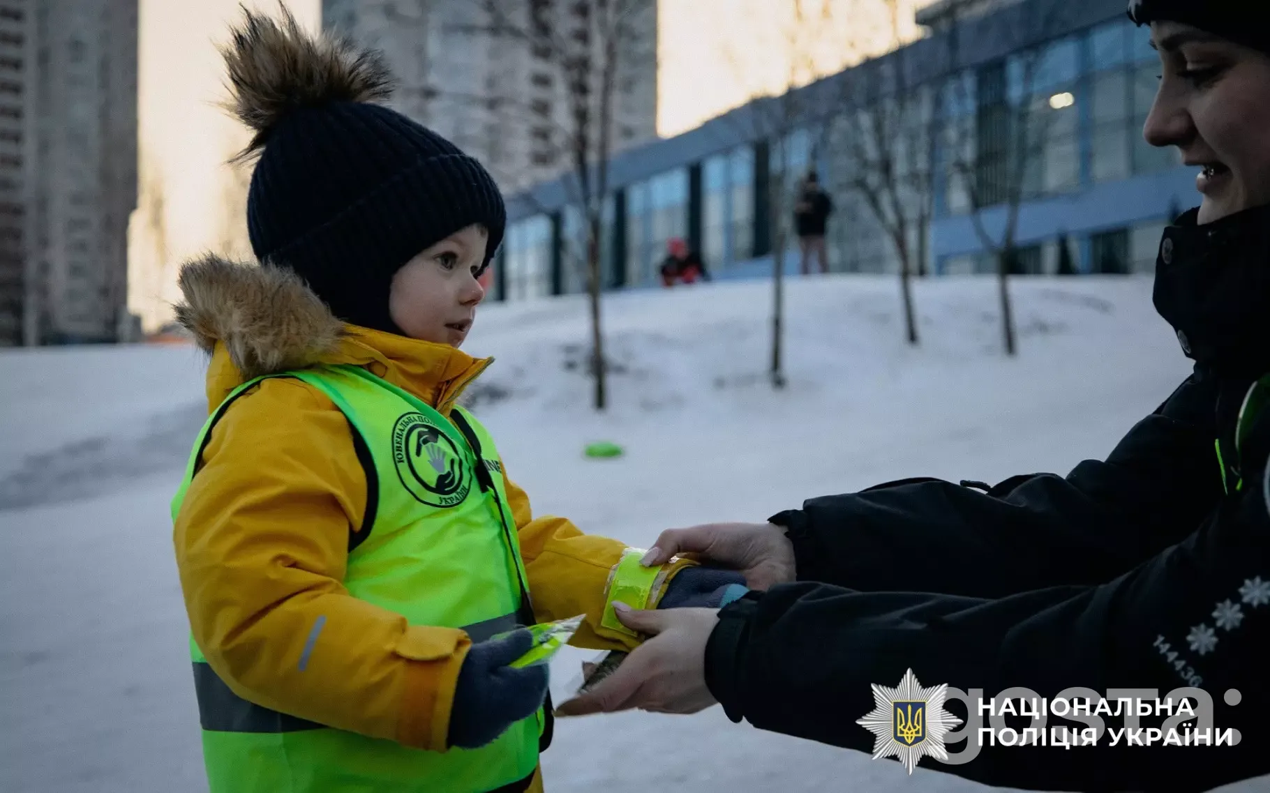 Ювенальні поліцейські роздають дітям світловідбивальні елементи для безпеки на зимових прогулянках у Києві.