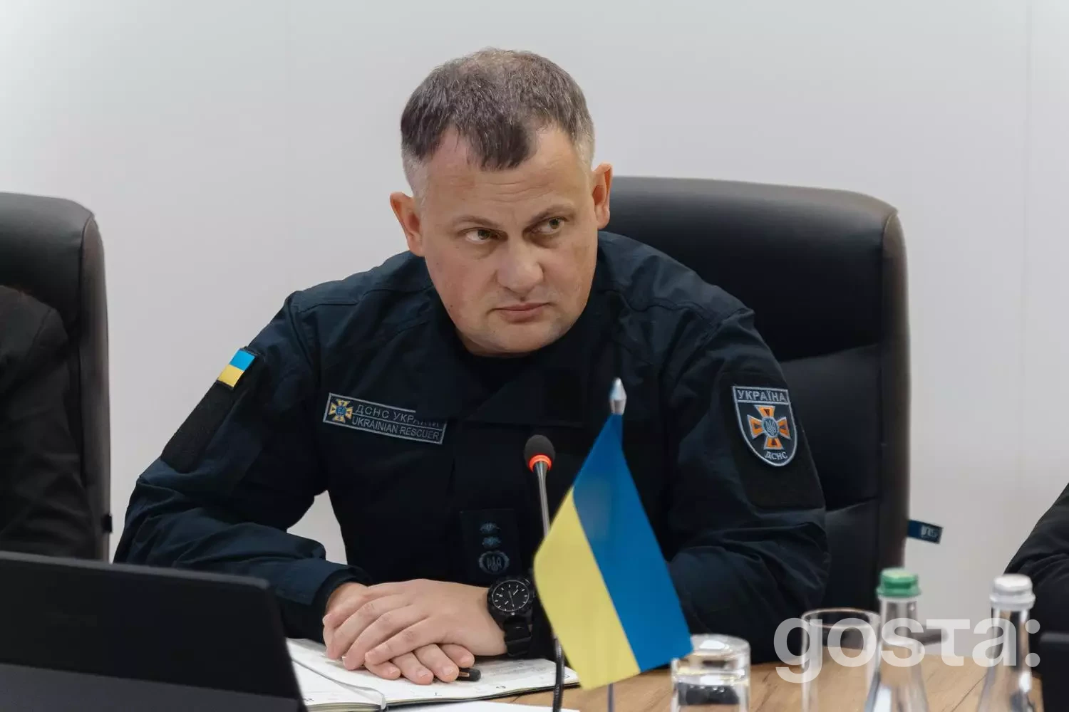 На фото зображено високопоставленого офіційного представника України під час зборів за столом, з українським прапором.