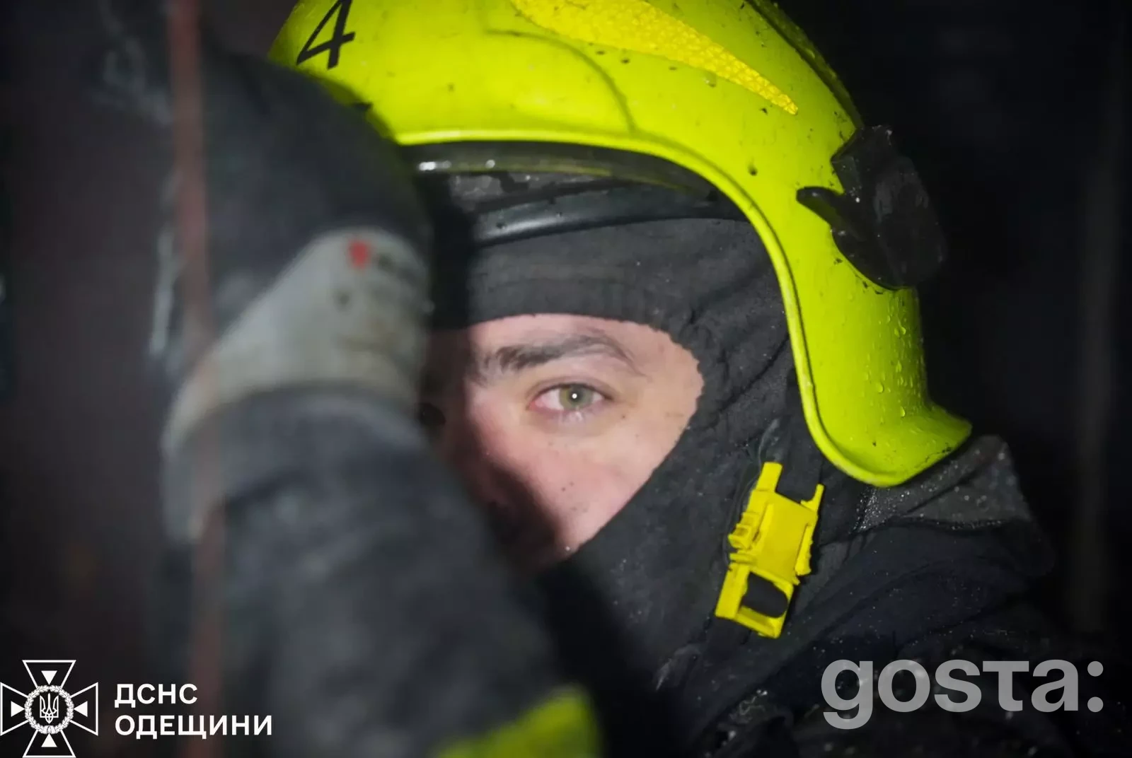 Рятувальник у жовтій касці працює на місці обстрілів в Україні, обличчя частково закрите, зосереджений вираз очей.