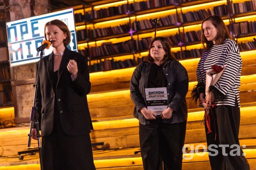 На церемонії Премії Читомо в Києві виступає жінка, тримаючи мікрофон, разом із двома іншими учасницями на сцені.