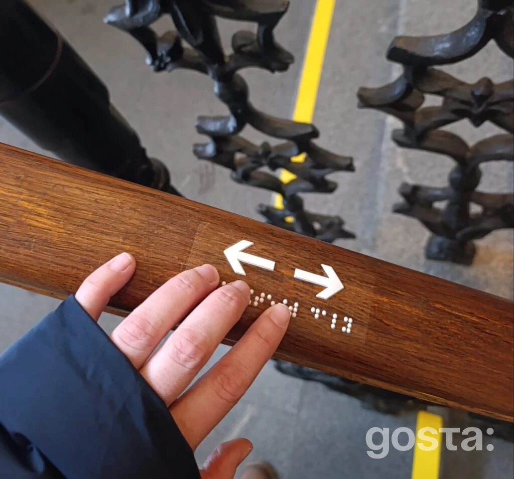 Людина читає тактильний вказівник шрифтом Брайля на поручні у Національній філармонії України.