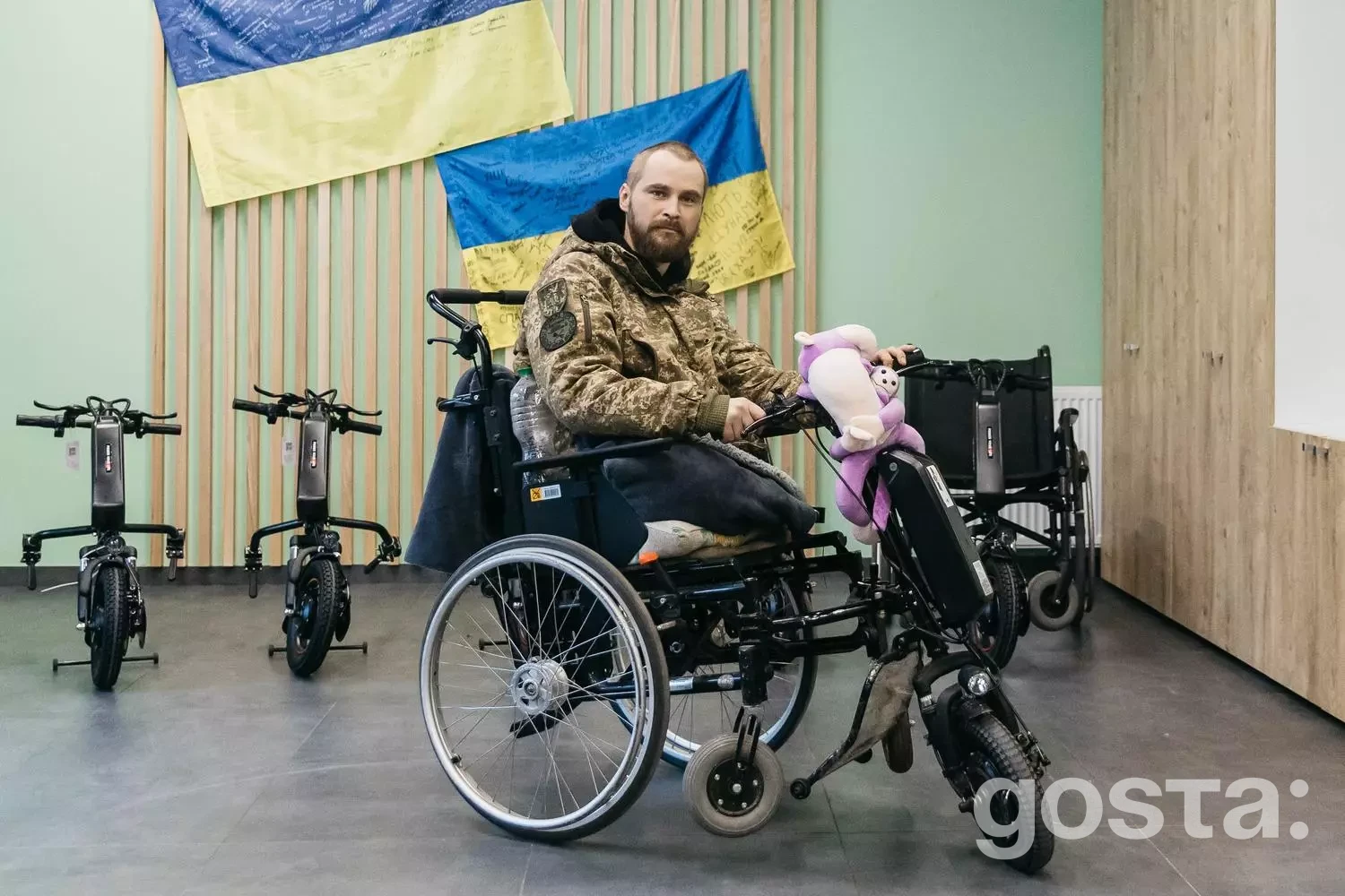 Чоловік у військовій формі на електровізку, поруч прапори України. Реабілітація ветеранів у медцентрі МВС України.