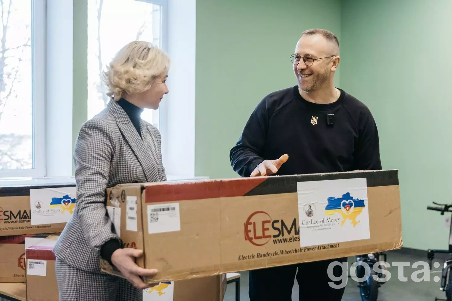 Двоє людей тримають коробку з електроприводами для колісних крісел у реабілітаційному центрі.