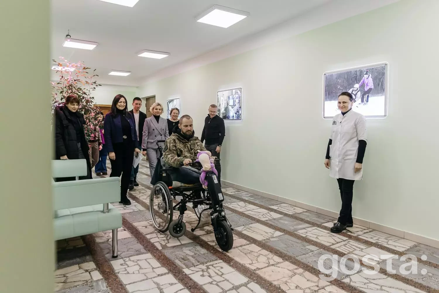 Користувач на інвалідному візку з електроприводом у клініці, супроводжуваний людьми, демонструє нову технологію реабілітації.