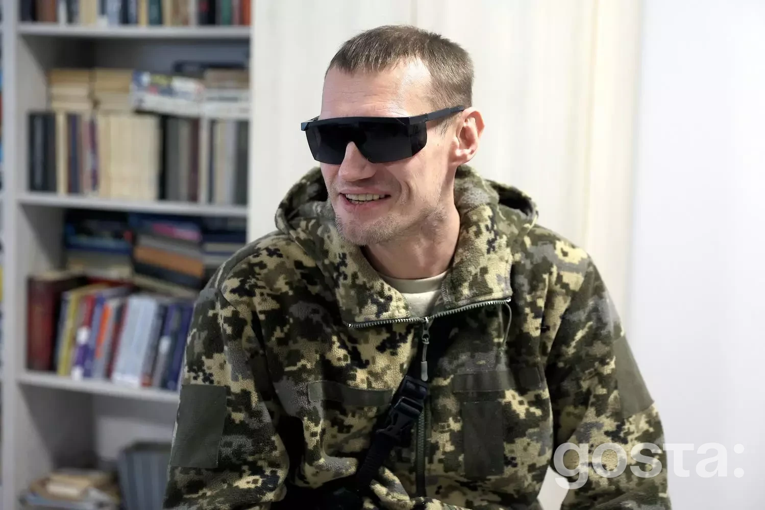 На зображенні ветеран у камуфляжі та темних окулярах, сидить у медичному реабілітаційному центрі.