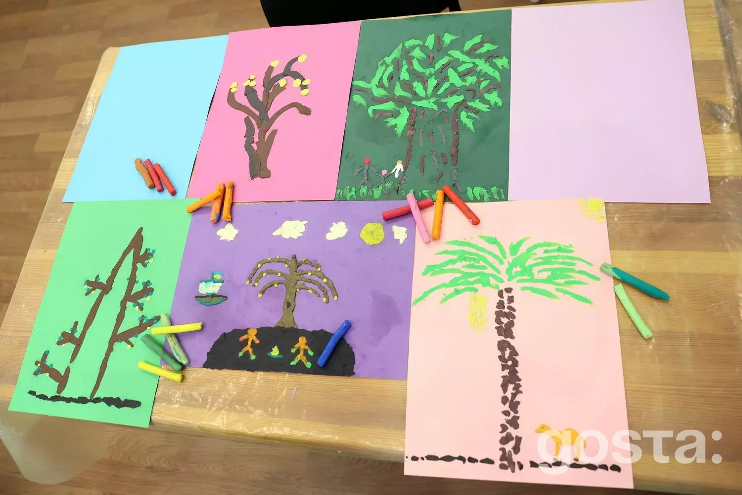 Малюнки дерев на кольоровому папері, оточені кольоровою крейдою на столі в рамках арт-терапії.