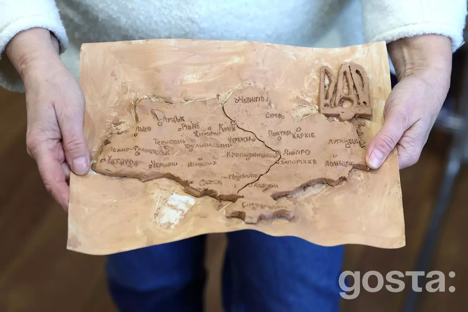 Людина тримає карту України, вирізьблену на дереві, символізуючи відданість і зв’язок з батьківщиною.