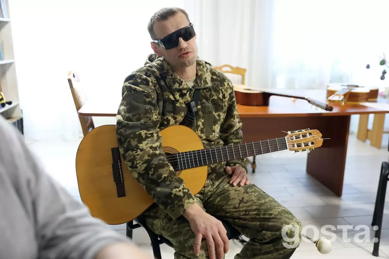 На зображенні ветеран у військовій формі з гітарою, що бере участь у музичній терапії для реабілітації.
