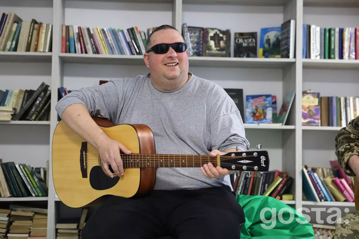 Чоловік у сонцезахисних окулярах грає на гітарі у медичному реабілітаційному центрі, Україна.