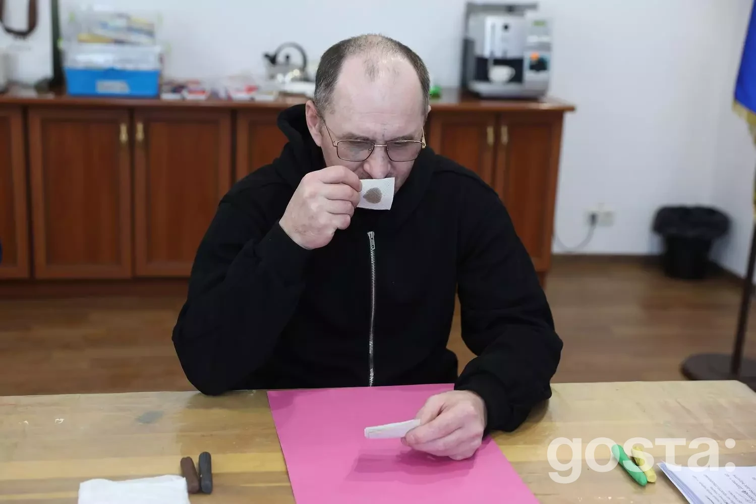 Людина у чорному светрі п'є напій у кімнаті реабілітаційного центру МВС України «Пуща-Водиця».